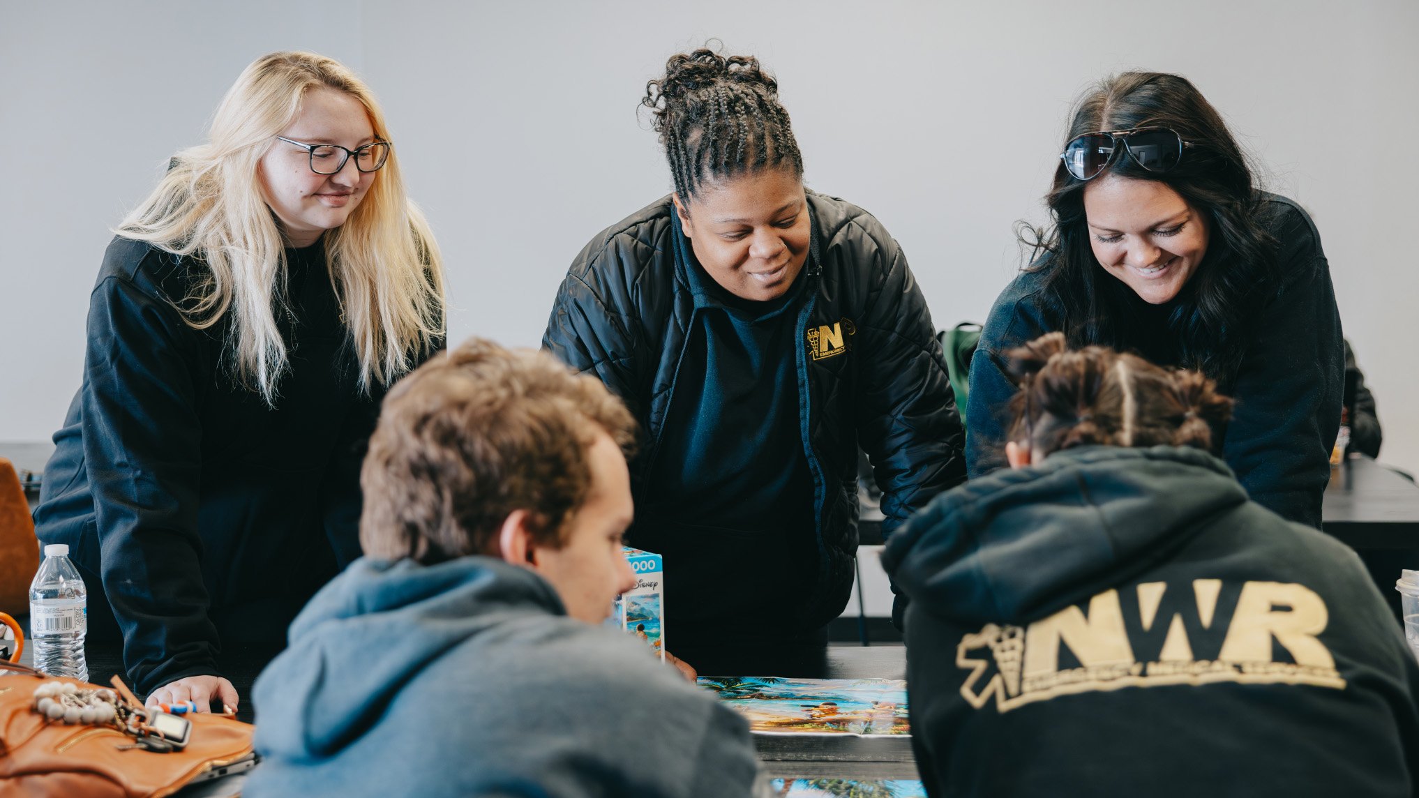 Five young adults gathered around a table working together on a jigsaw puzzle.
