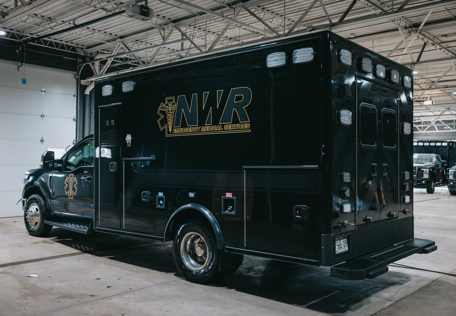 Black NWR Emergency Medical Services ambulance parked inside a spacious garage.