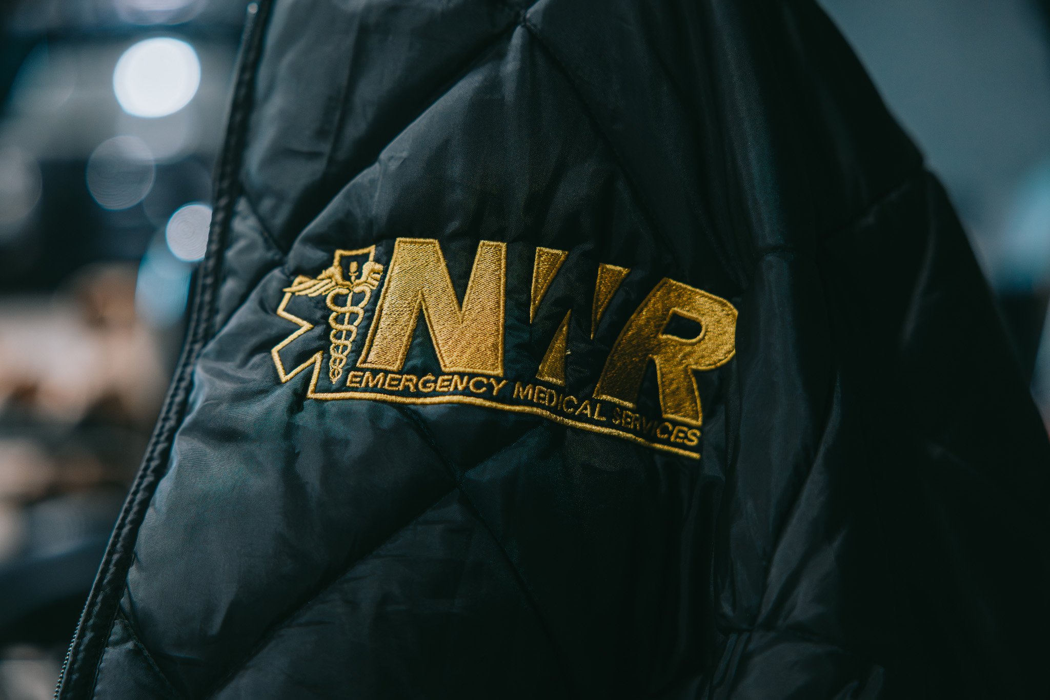 Black jacket with gold embroidered text and medical symbol reading NWR Emergency Medical Services.