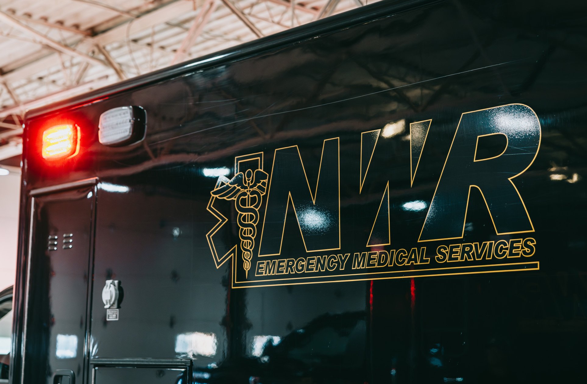 Side view of a black Emergency Medical Services vehicle with red taillight and EMS emblem.