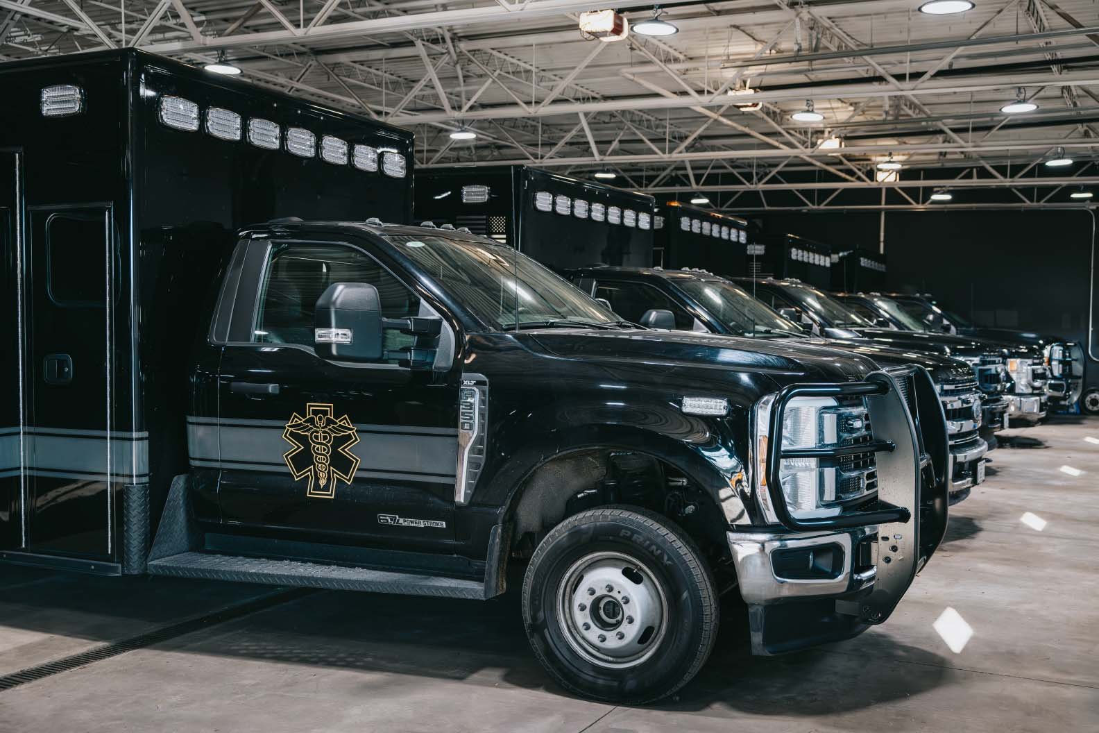 Row of black emergency medical service trucks parked indoors, with one prominently showing a gold Star of Life emblem on the door.