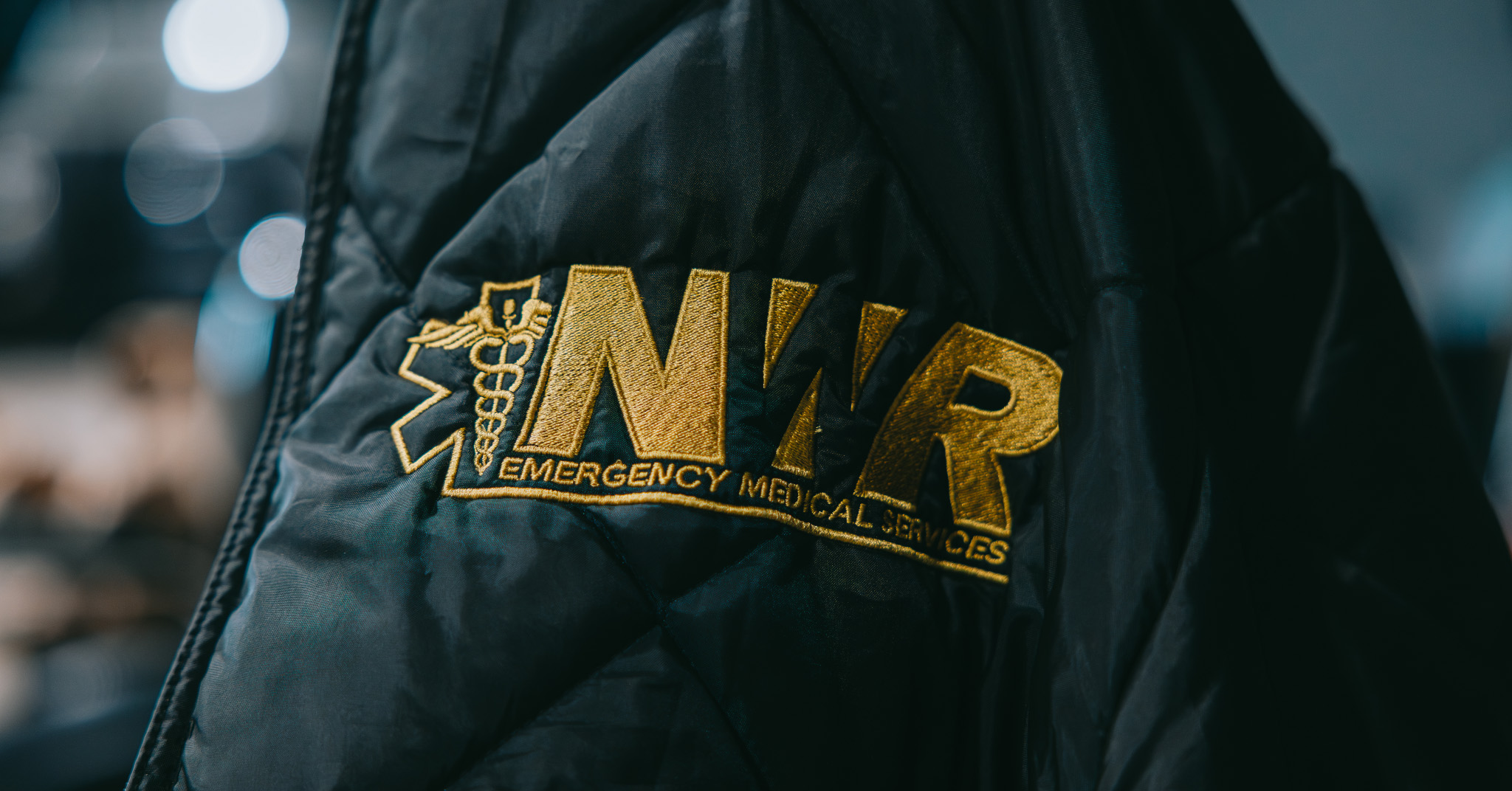 Black jacket with gold embroidered logo reading 'NWR Emergency Medical Services' and a medical caduceus symbol.
