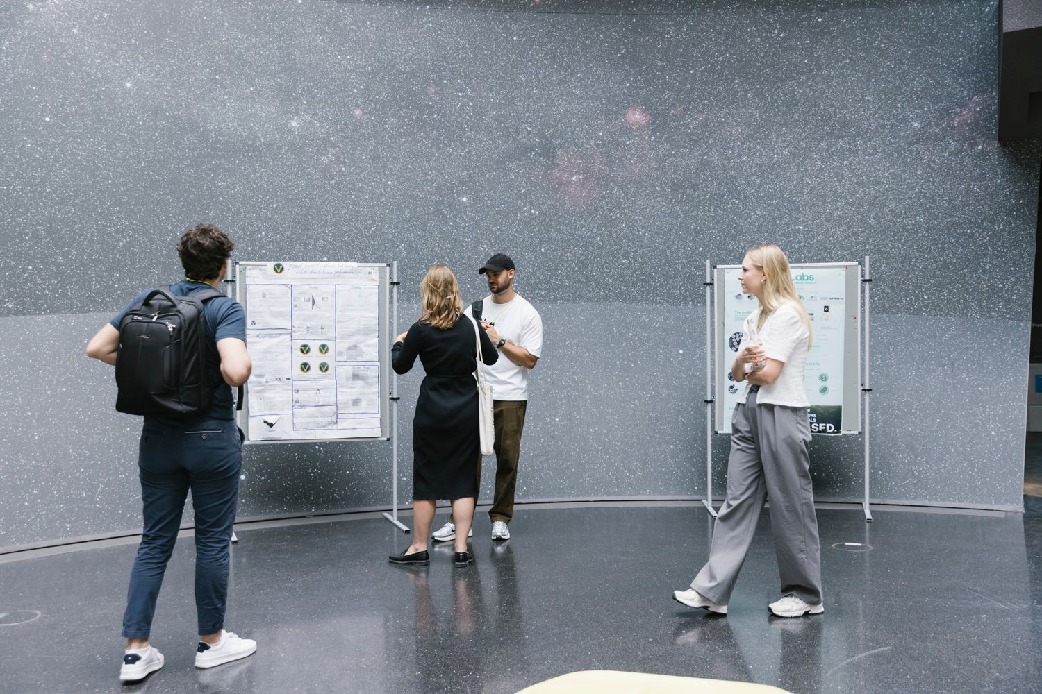 Four people are viewing and discussing research posters displayed on stands.