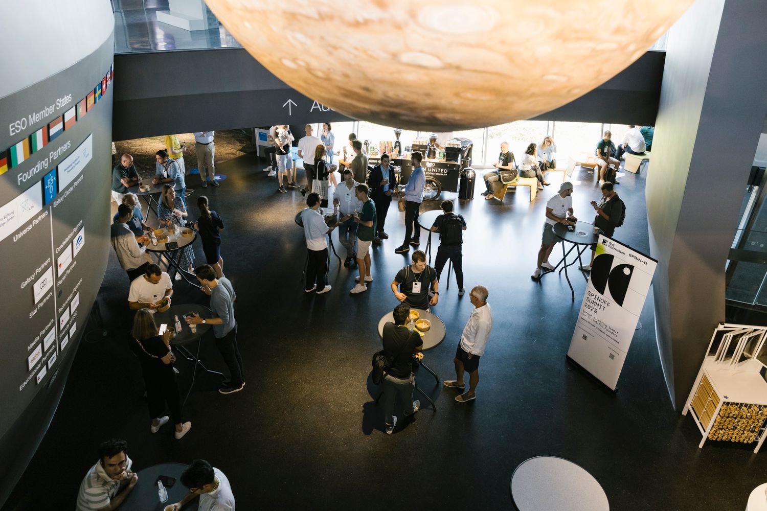 Founders, scientists, industry experts, and investors mingling and chatting in a relaxed setting with a large planet model overhead.