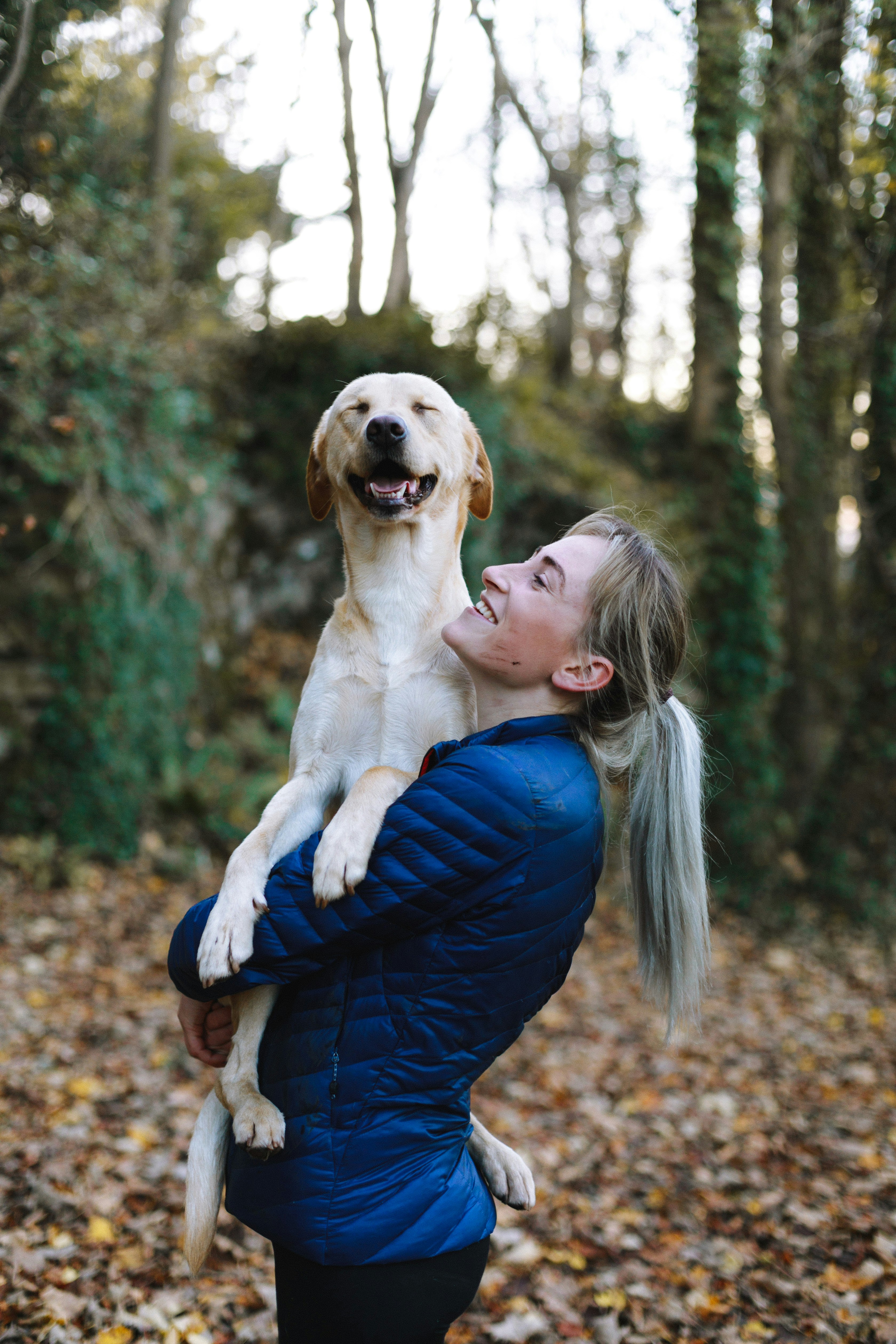 Une femme en veste bleu câline un chien qu'elle porte dans ses bras
