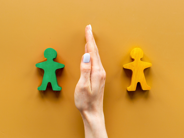Eine Hand trennt zwei unterschiedlich farbige Holzfiguren voneinander – als Symbol für Konflikte, unterschiedliche Positionen und zwischenmenschliche Spannungen.