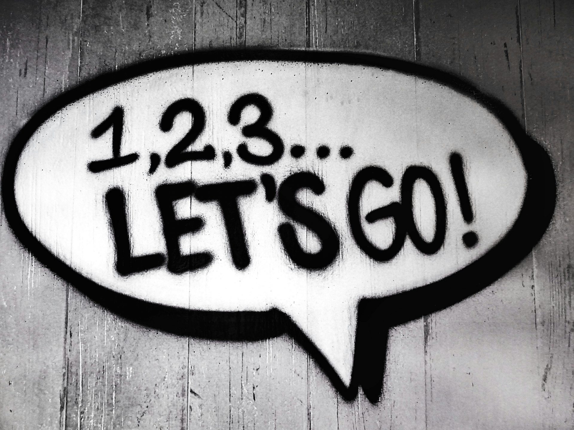Graffiti-Sprechblase mit der Aufschrift „1,2,3... Let’s go!“ auf grauer Wand.