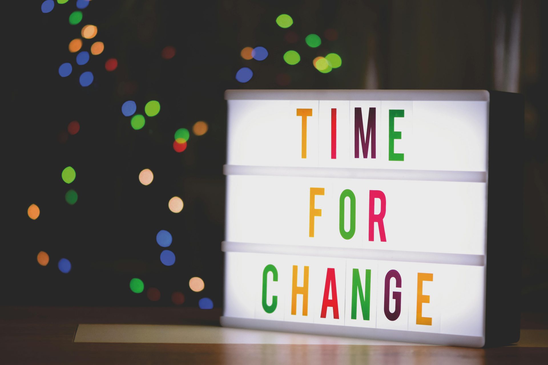 Leuchtbox mit der Aufschrift „Time for Change“ vor unscharfen bunten Lichtern als Symbol für Veränderung und Aufbruch.