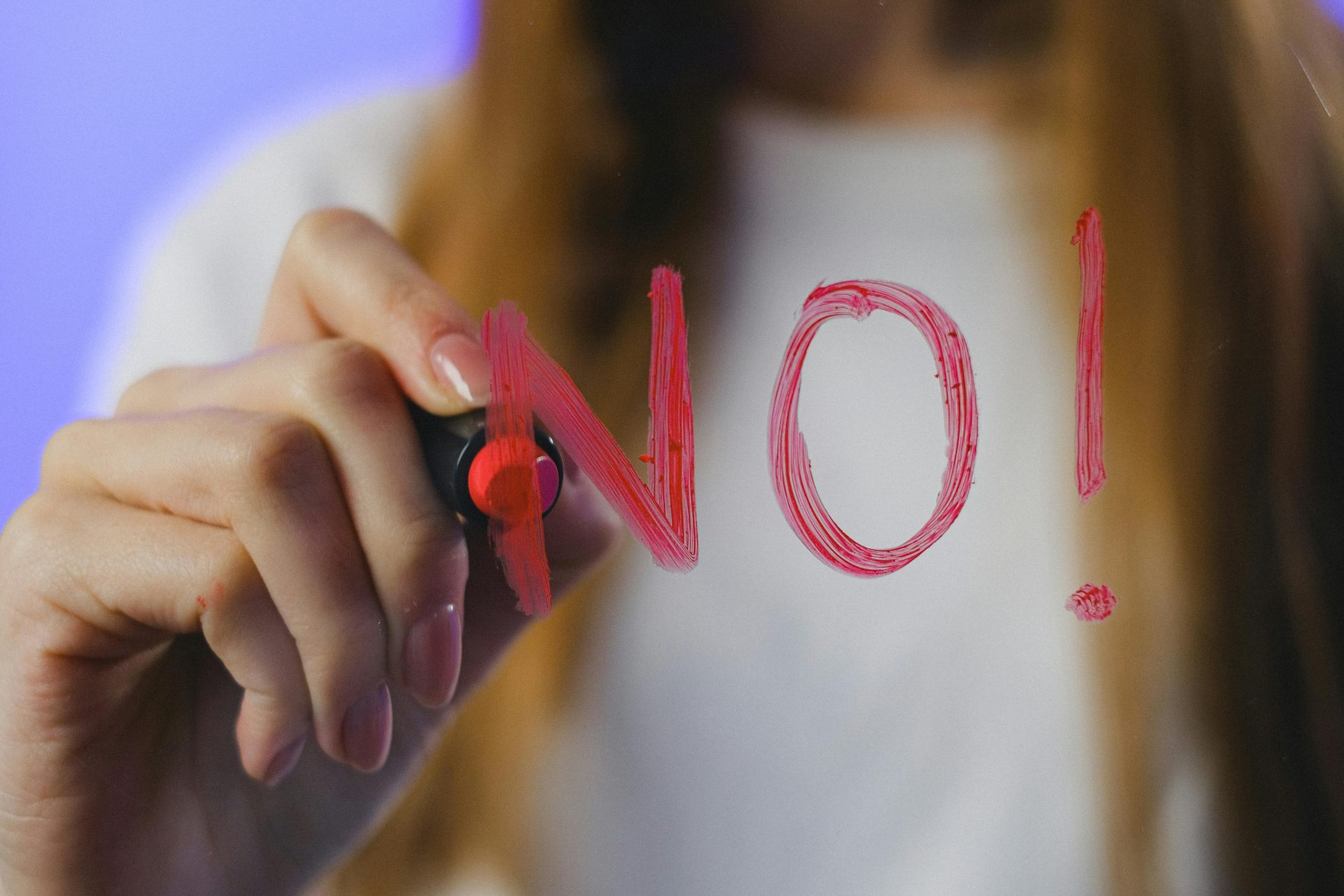 Person schreibt mit rotem Marker das Wort „NO!“ auf eine Glasfläche als Symbol für klare Grenzen und Nein-Sagen.