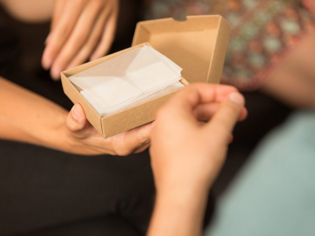 Eine Person hält eine kleine geöffnete Schachtel mit einem kleinen Geschenk in den Händen.