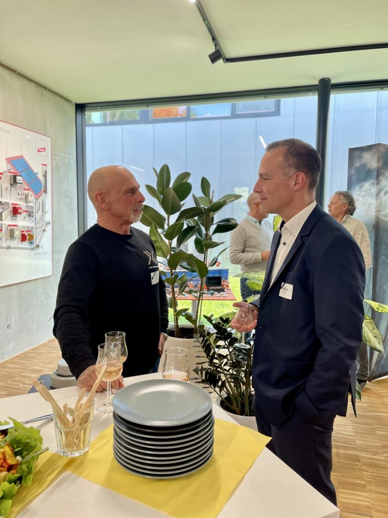 Zwei Männer unterhalten sich bei der Veranstaltung an einem Stehtisch mit Getränken und Buffet.