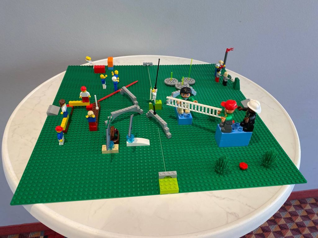 LEGO Serious Play Modell auf einem Tisch mit Figuren, Symbolen und Verbindungselementen zur Darstellung von Team- oder Prozessstrukturen.