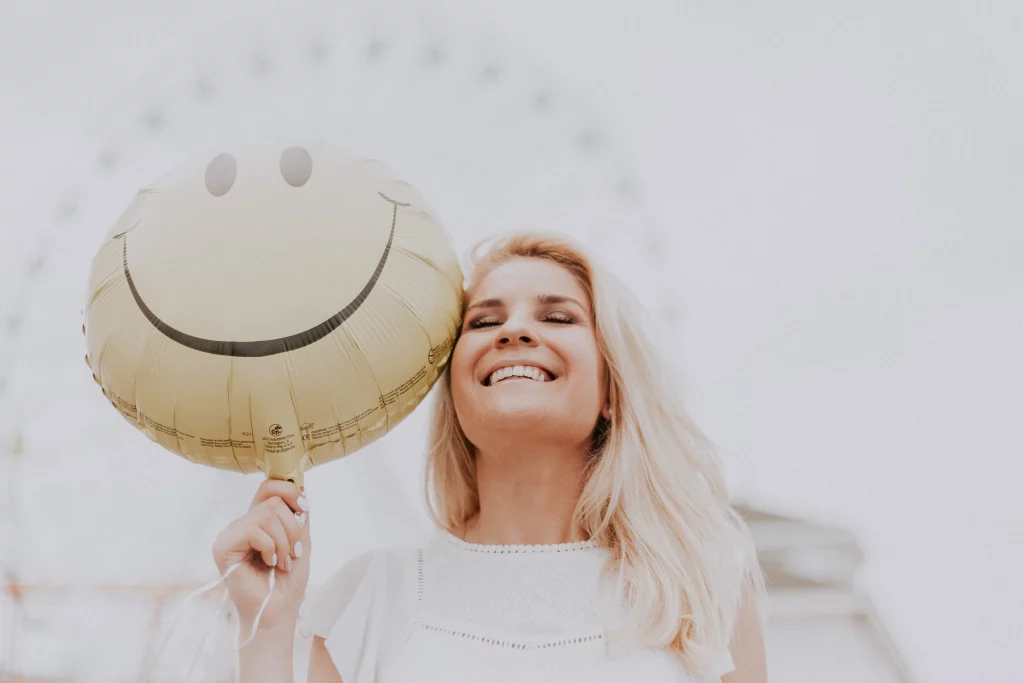 Lachende Frau hält einen goldenen Luftballon mit Smiley-Gesicht und vermittelt Freude und positive Stimmung.