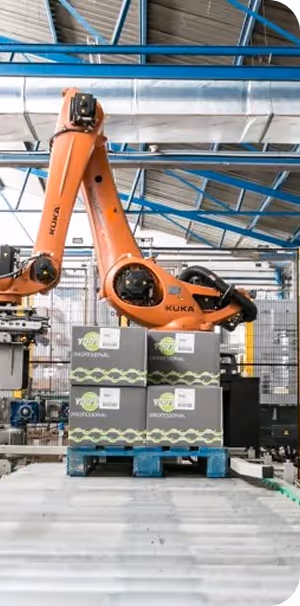 Brazo robótico naranja KUKA manipulando cajas de productos en una línea de producción industrial.