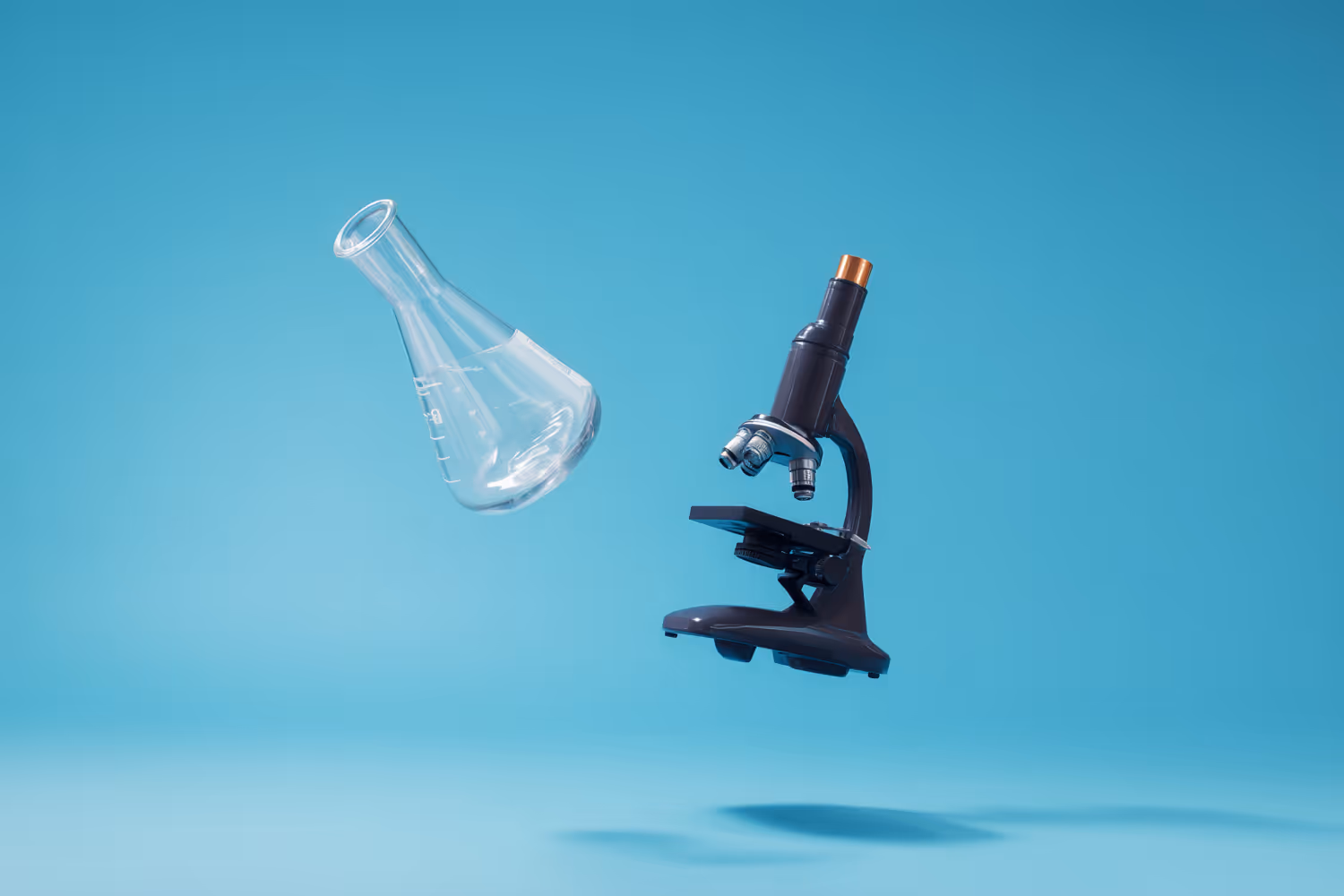 Un microscopio negro y un matraz de laboratorio de vidrio flotando sobre un fondo azul.