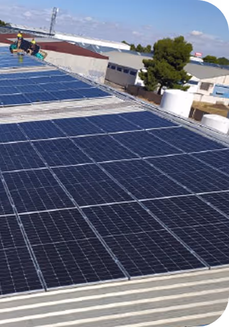 Paneles solares instalados en el techo de un edificio industrial con dos trabajadores usando cascos amarillos.