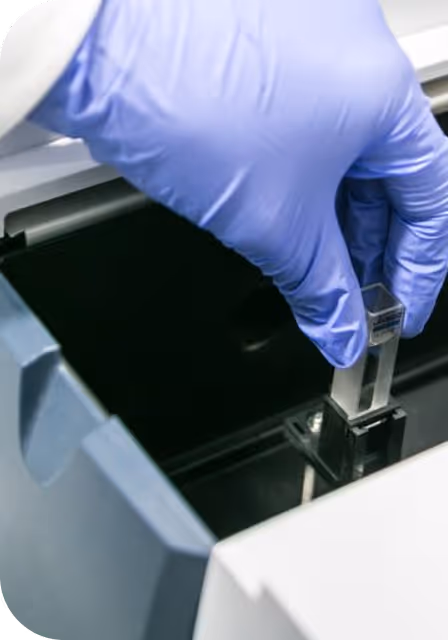Mano con guante azul manipulando una cubeta de muestra transparente en equipo de laboratorio.