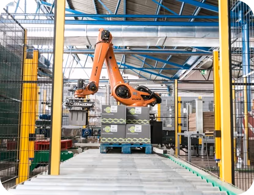 Brazo robótico naranja KUKA automatizando el paletizado de cajas en una línea de producción industrial.