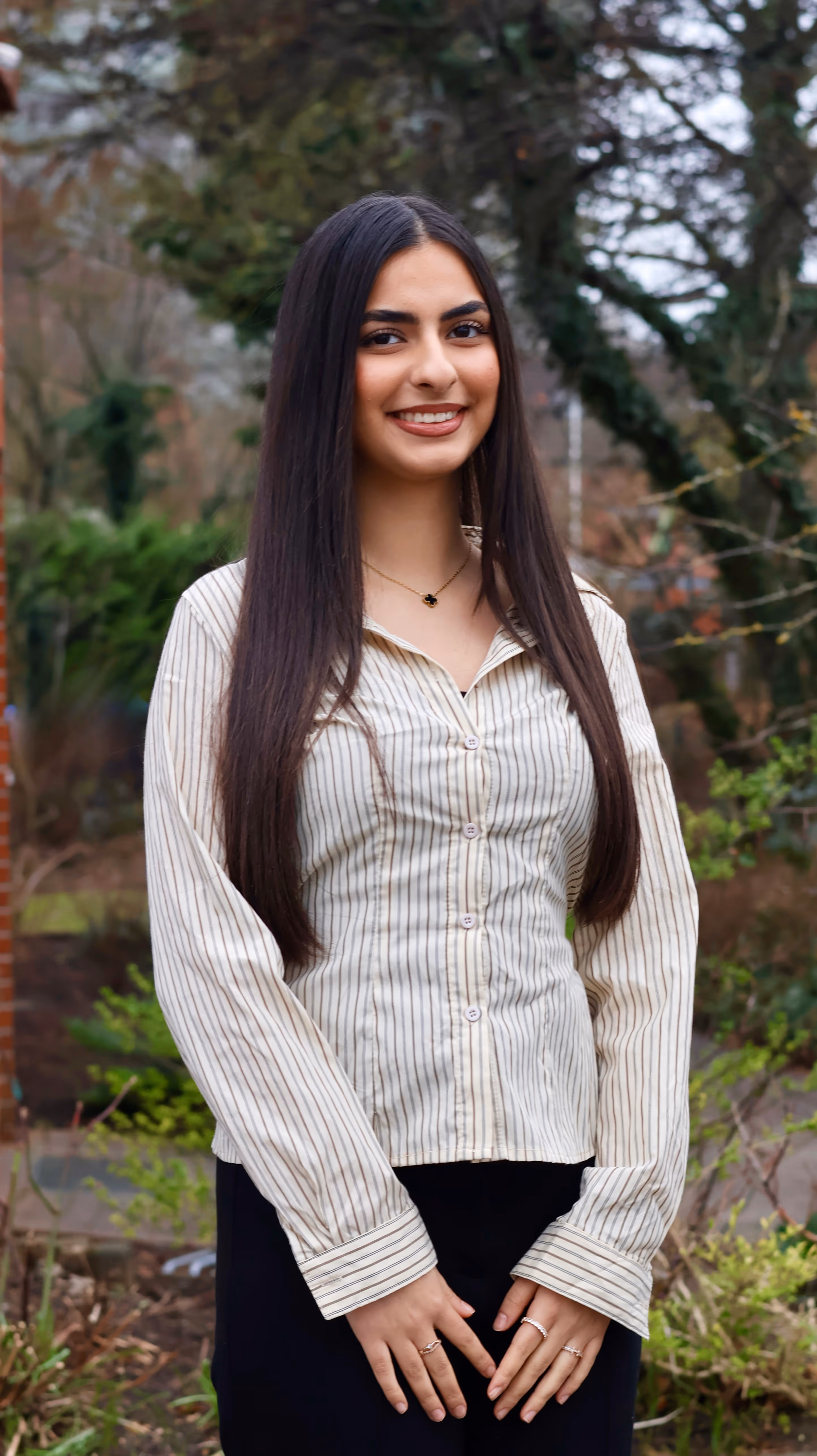 Lächelnde Frau mit langen Haaren, die nach vorne zeigt, trägt eine helle Strickjacke mit Trompetenärmeln.