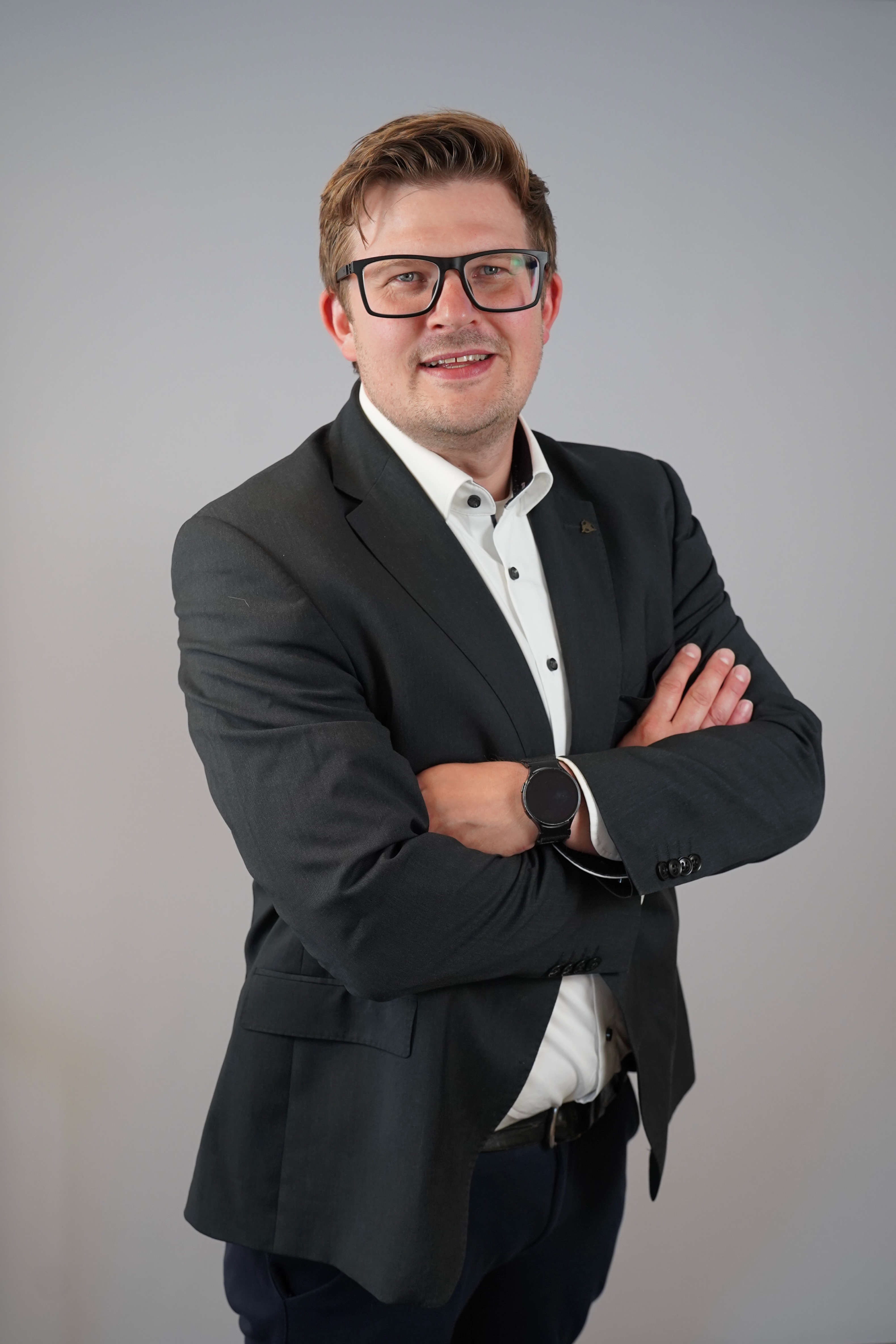 Porträt eines lächelnden Mannes mit Brille, der einen Anzug im Freien trägt.