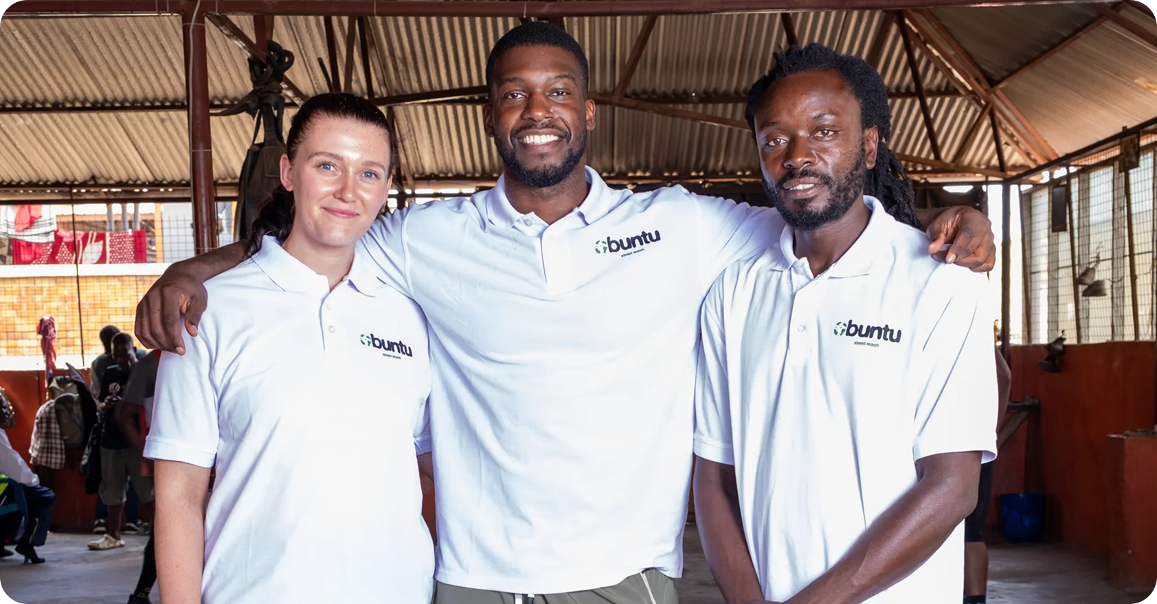 Three people wearing white polo shirts with 'Buntu' logo posing together inside a large open structure.