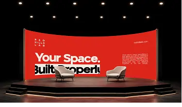 Stage with two modern chairs in front of red curved screen displaying real estate branding text.