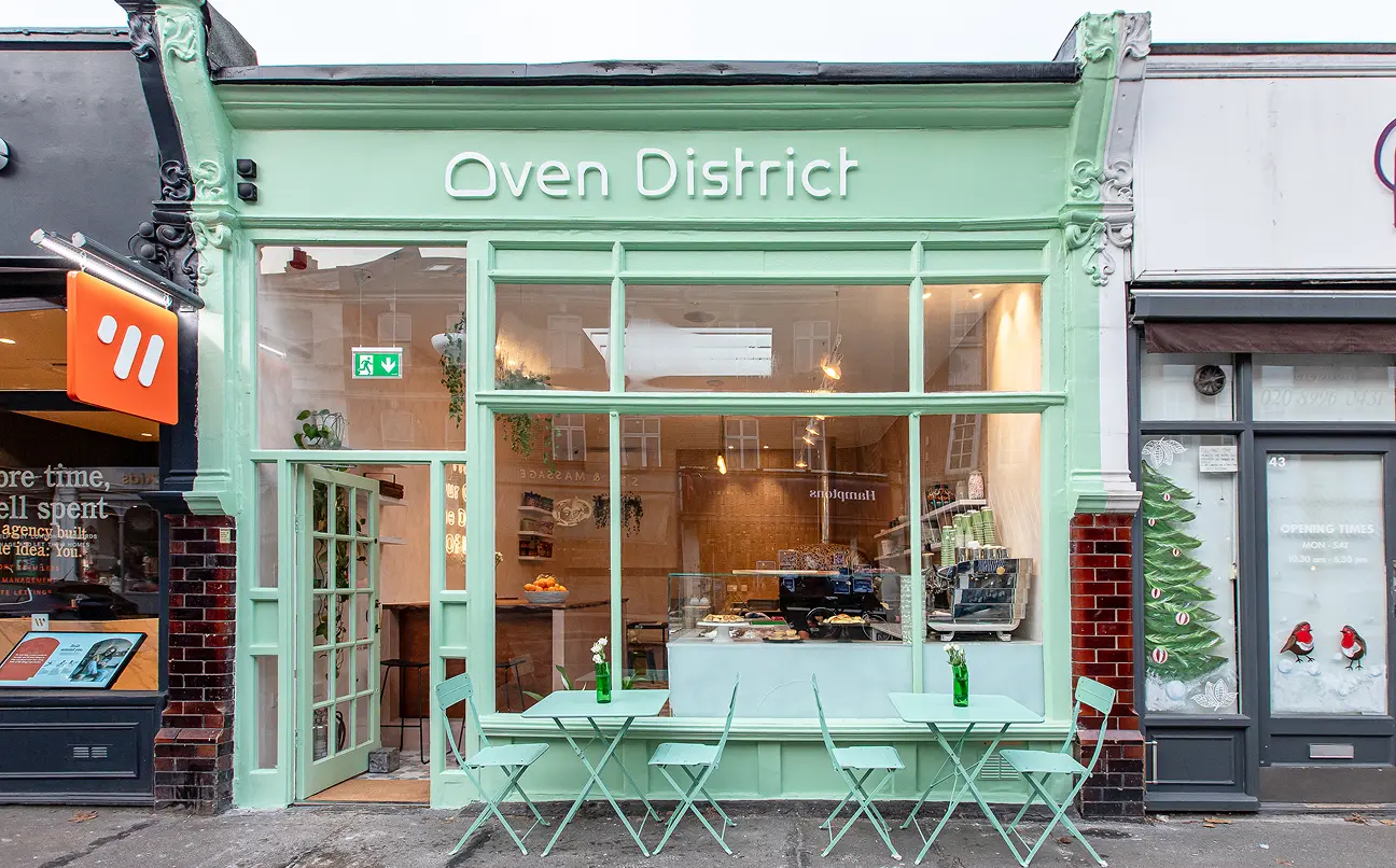 Mint-green facade of Oven District cafe with tables, chairs, and large front window display.