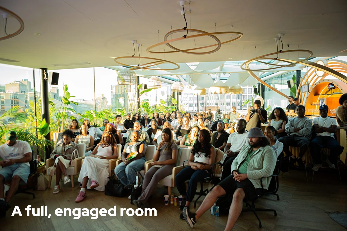 A diverse group of people attentively seated in a bright, modern room with large windows and plants.