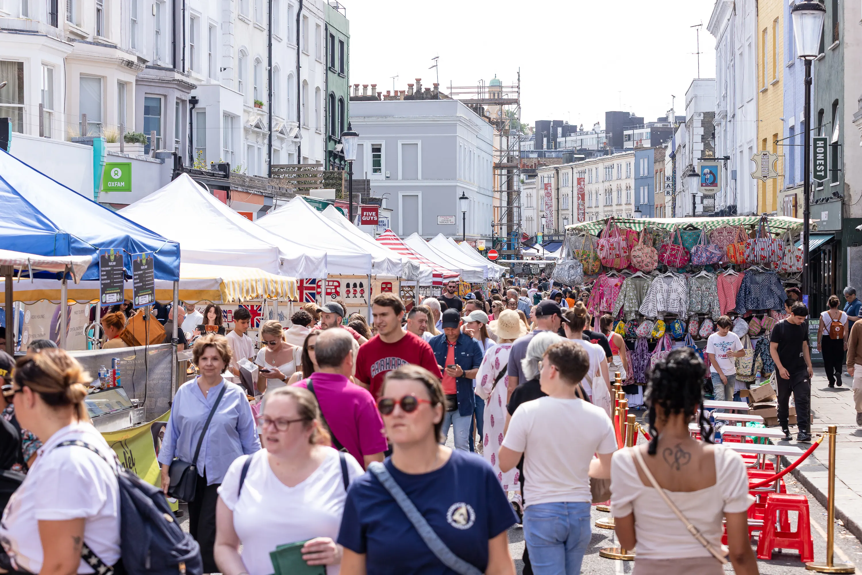Busy street market with people walking among stalls selling bags and goods in a city setting.