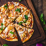 Sliced pizza with chicken, onions, and cilantro on a wooden board.