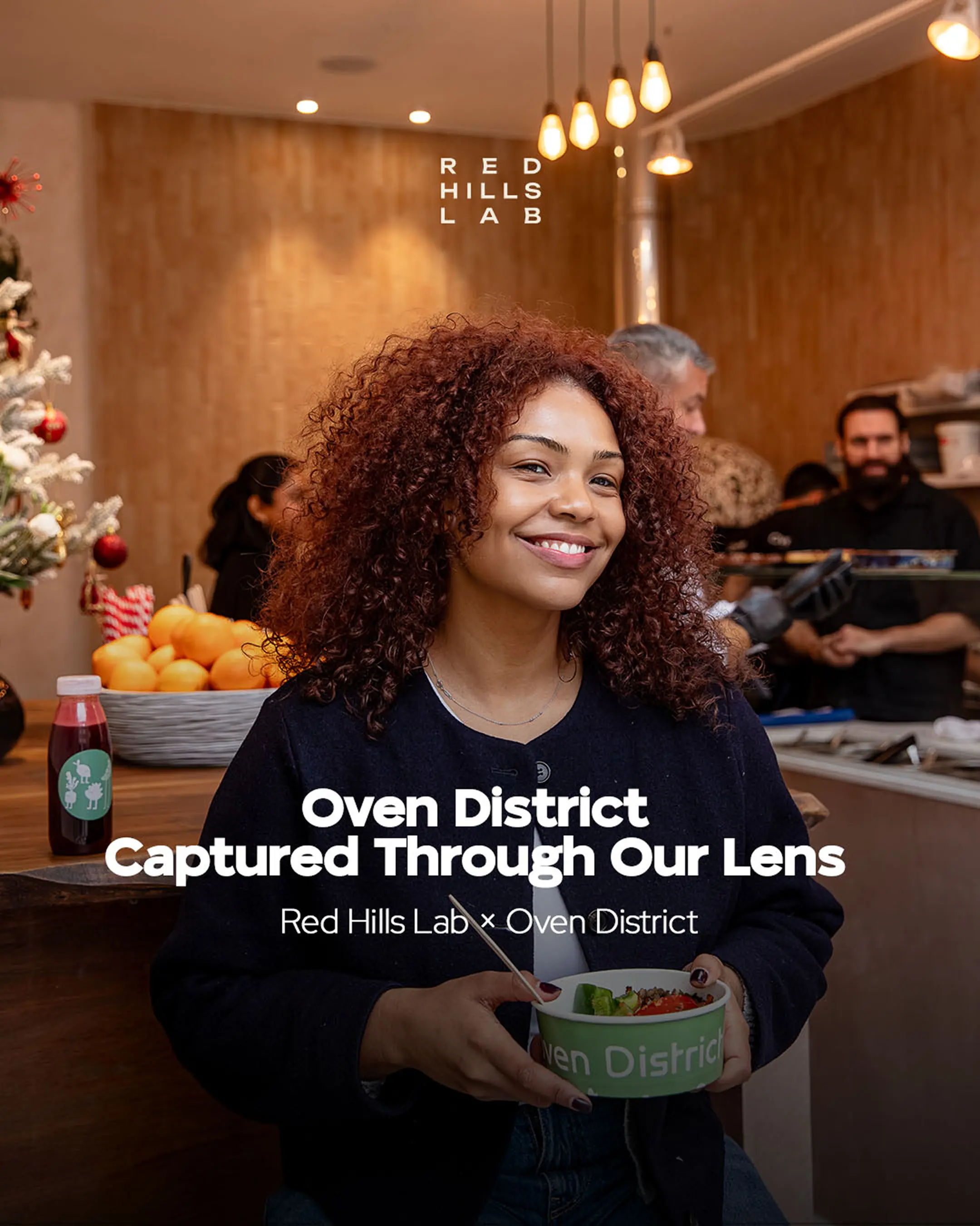 Smiling woman holding a bowl of food inside a cozy eatery with wooden interior and hanging lights.