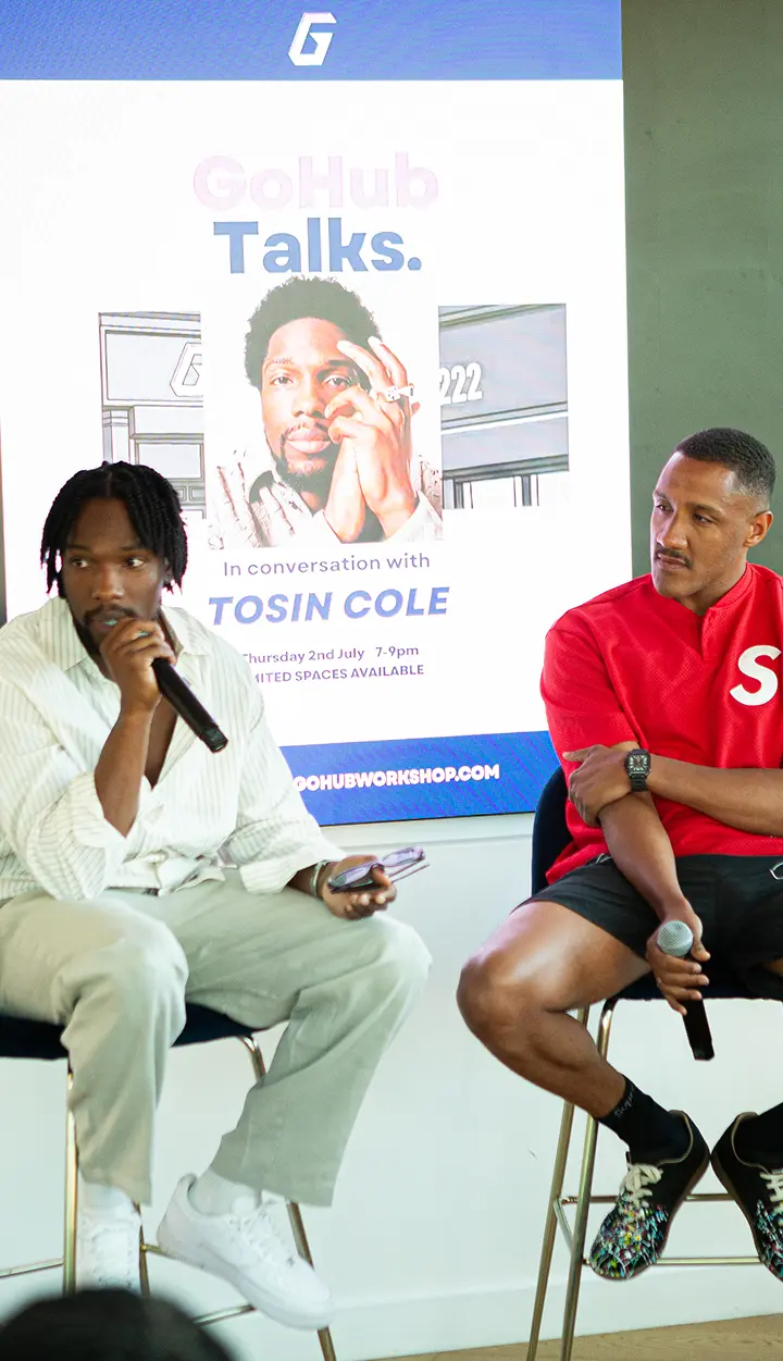 Two men seated with microphones in front of a GoHub Talks poster featuring Tosin Cole.