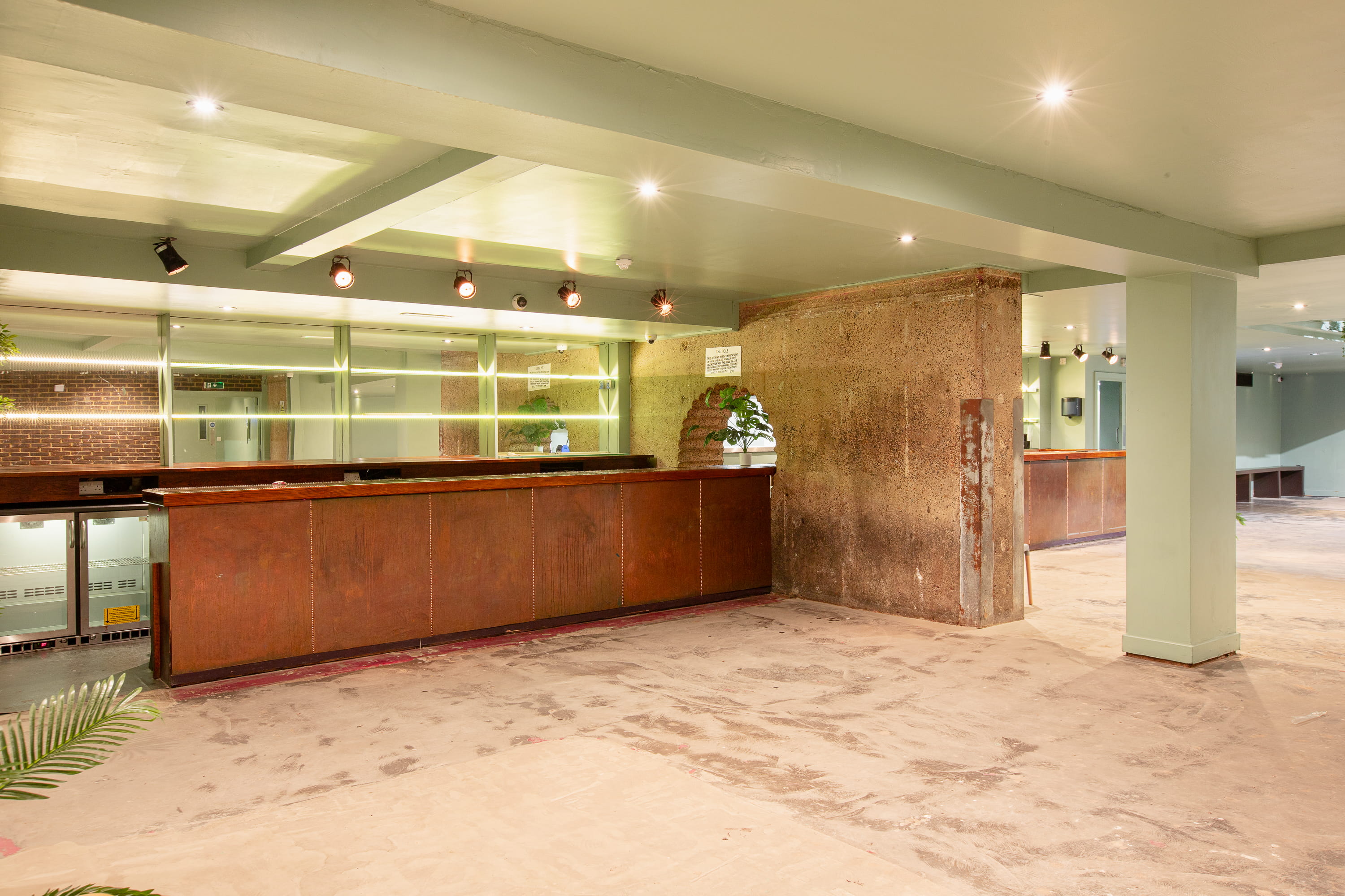 Empty interior space with exposed concrete wall, wooden counters, glass panels, and ceiling lights.