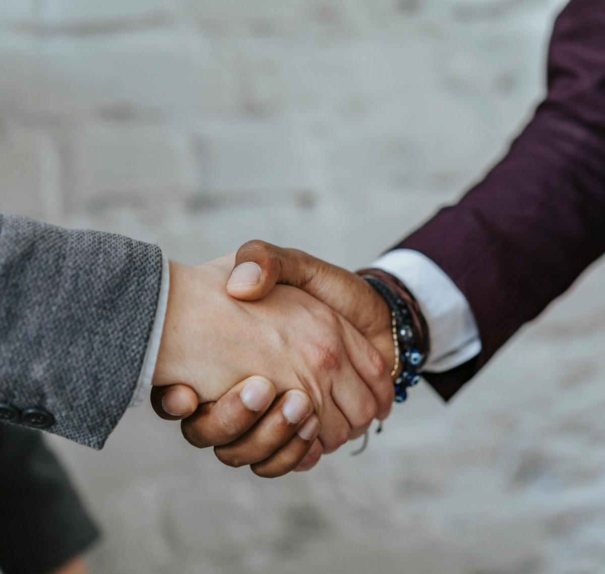 Two people shaking hands, one wearing a gray suit and the other a burgundy suit with bracelets.