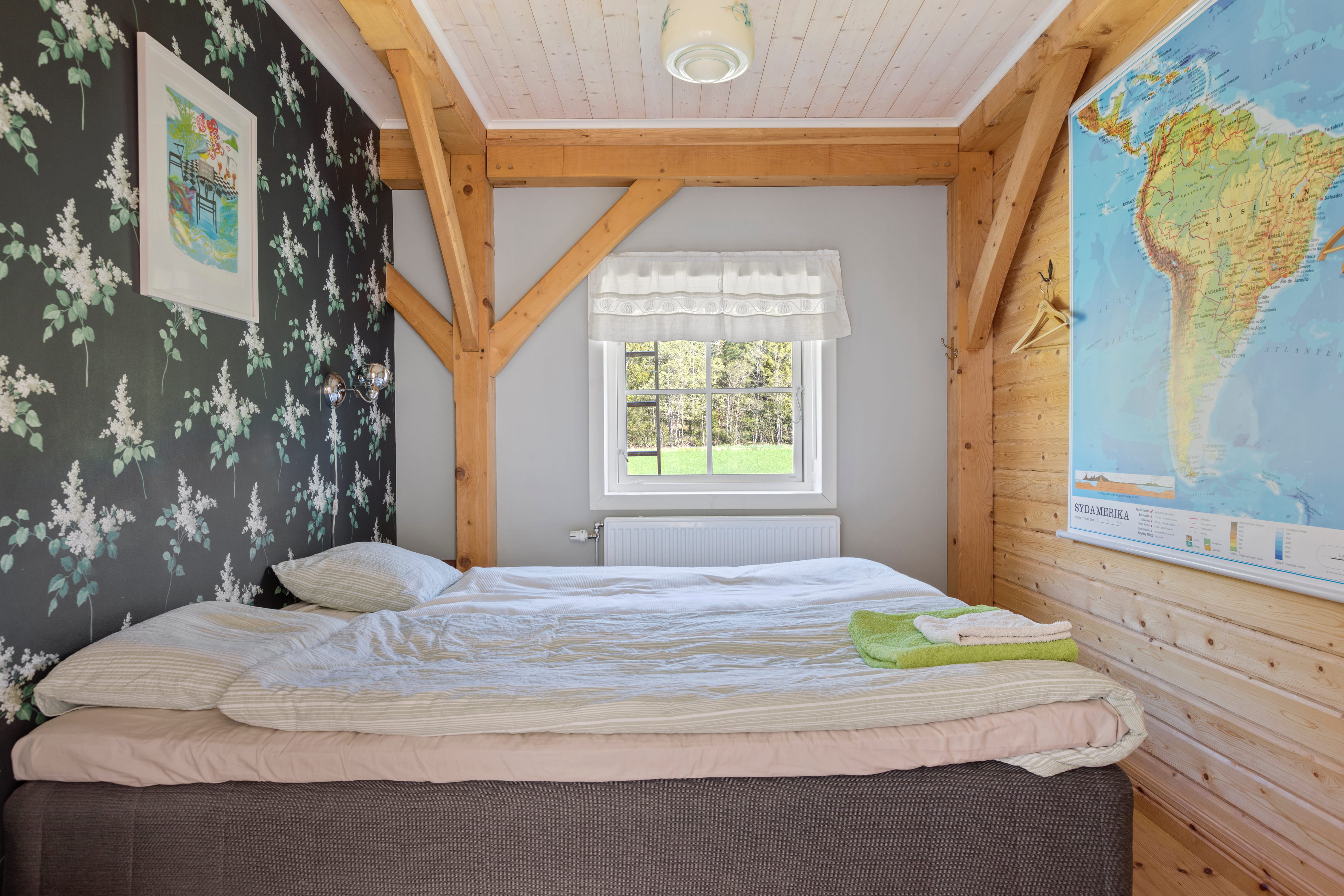 Cozy, modern living room with angled wood beams, large windows, a light gray sofa, and a decorative glass coffee table. Greenery visible outdoors.