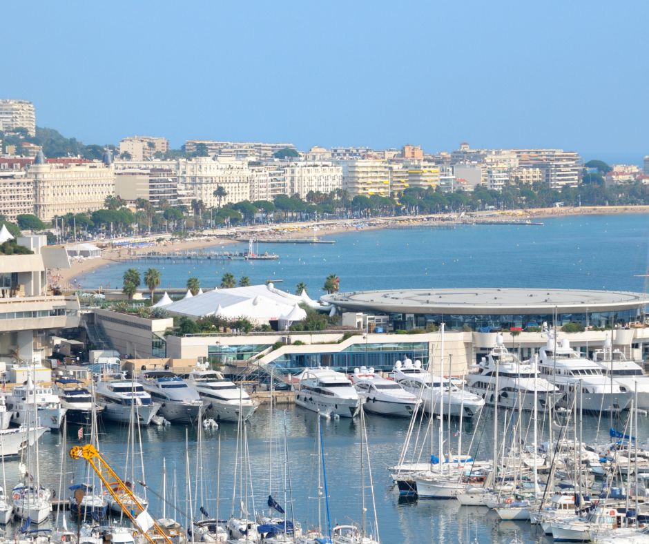 A marina filled with numerous yachts and sailboats, with a cityscape and beachfront in the background under a clear blue sky.
