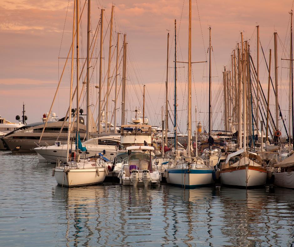 Numerous sailboats and yachts docked closely together in a marina at sunset with calm water reflecting the boats.