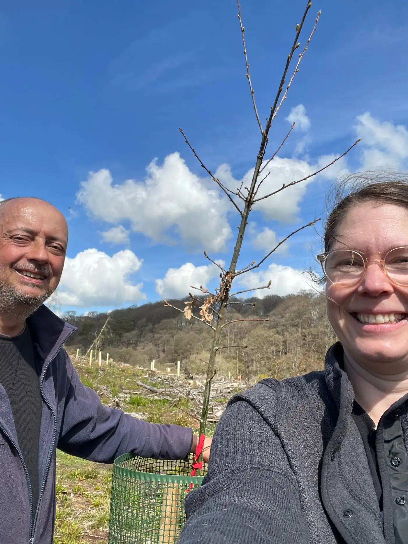Couple holding a tree sapling together with forest backdrop.