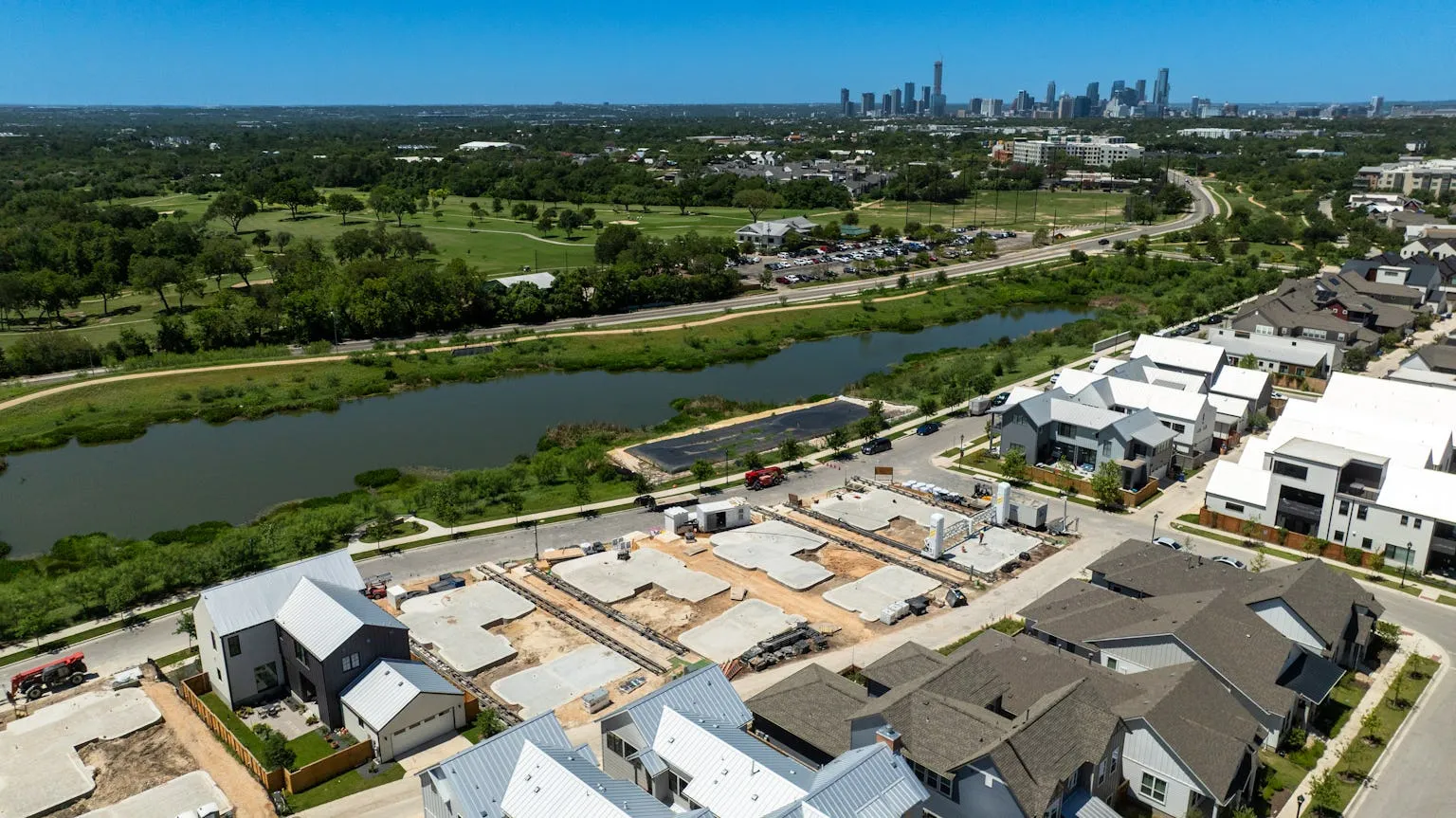 Aerial view of riverfront neighborhood with concrete foundations and tracked printer rails for 3D-printed homes