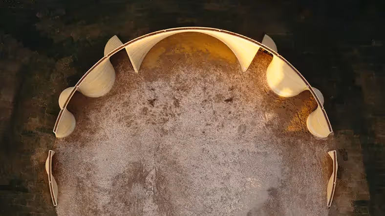 Aerial view of curved 3D-printed walls forming a semicircular enclosure on bare soil.