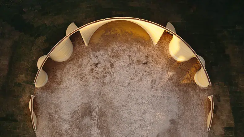 Aerial view of curved 3D-printed walls forming a semicircular enclosure on bare soil.