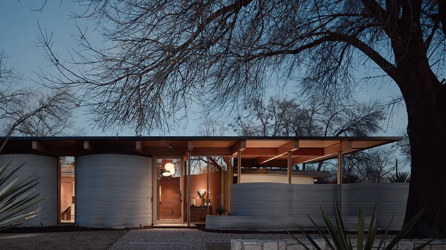 Single-story modern home with curved concrete walls and glass entrance at dusk