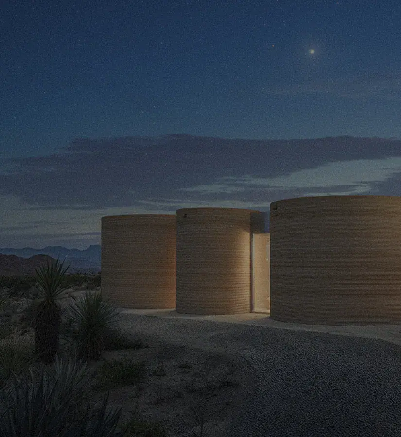 Three cylindrical buildings lit at night in a desert landscape under a starry sky