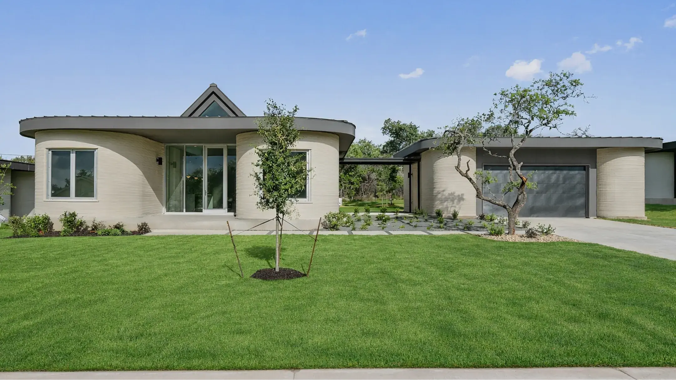 Modern 3D-printed home with curved walls, central glass entrance, garage and front lawn