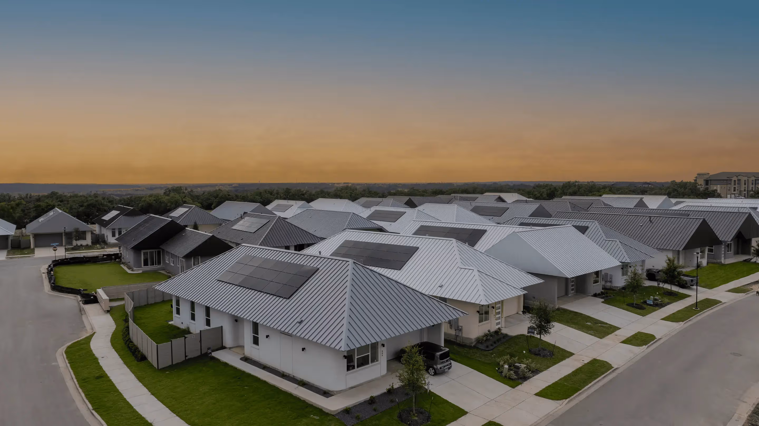 Aerial view of modern single-story homes with metal roofs and solar panels at sunset