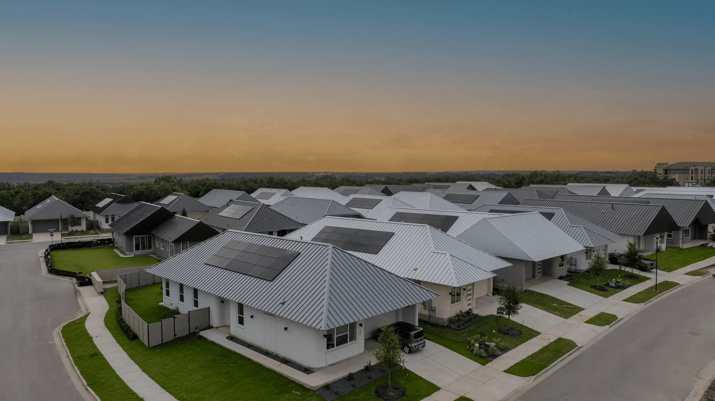 Aerial view of modern single-story homes with metal roofs and solar panels at sunset
