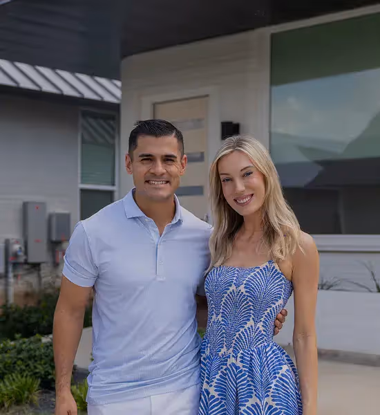 Man and woman smiling in front of a modern house