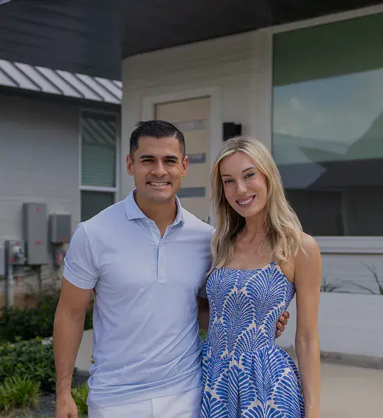 Man and woman smiling in front of a modern house