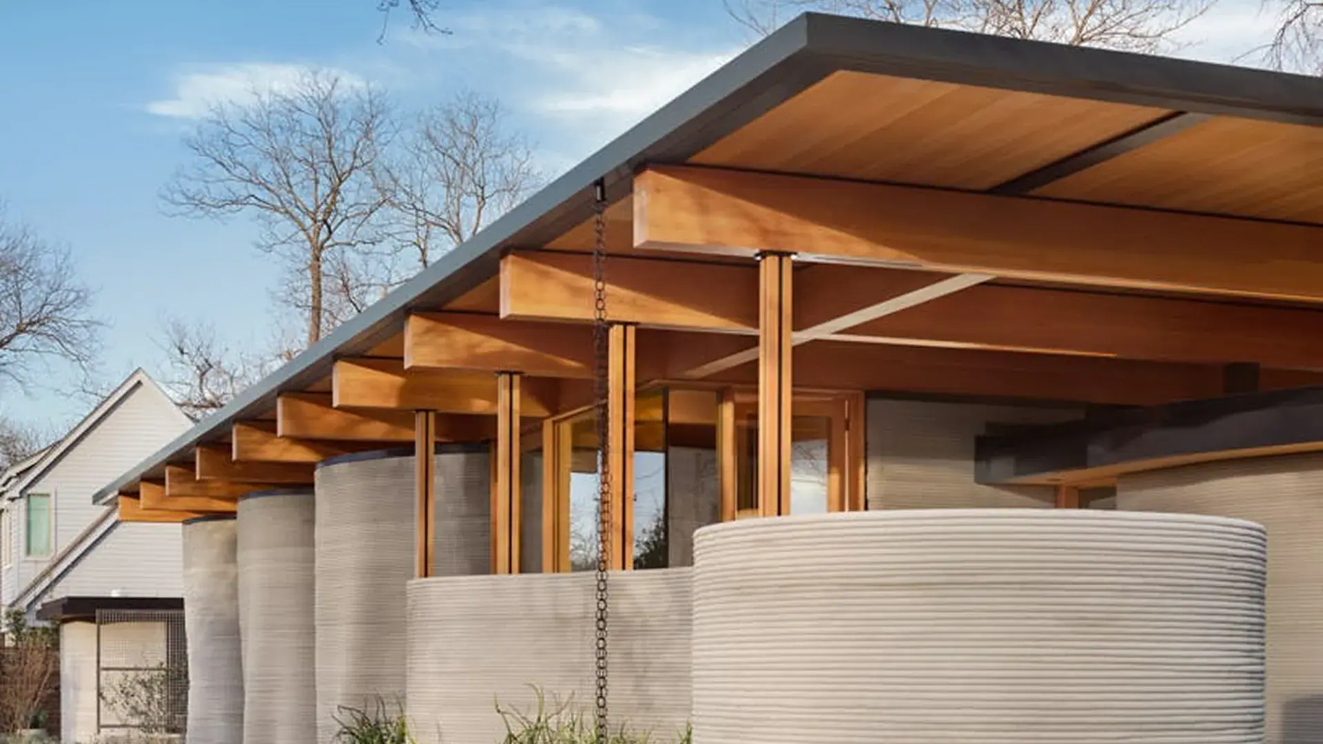 Modern porch with wooden beams, rain chain, and cylindrical 3D-printed concrete walls