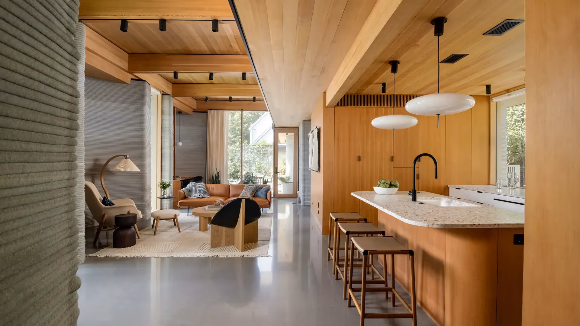 Open-plan living room and kitchen with wood ceiling, terrazzo island, leather sofa and bar stools